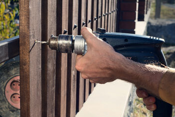 Man's hand holding power tool and working on a wooden fence in Cambridge, Ontario